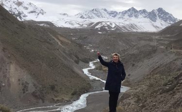 Woman stands in front of stream with mountains in the background