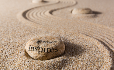 Stone in sand with engraving reading 'Artswork inspires'.
