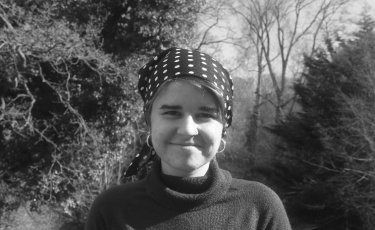 Ilyayda Kalach, wearing polka dotted bandana with a red sweater, forest in the background, monochrome image
